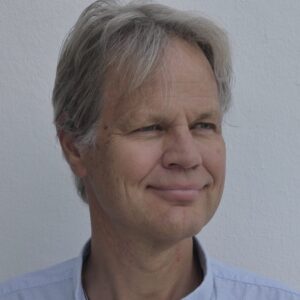 Gottfried Leibbrandt, voormalig CEO van SWIFT, kijkt rustig opzij tegen een neutrale, zakelijke achtergrond.