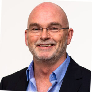 John Visser, voormalig adjunct-directeur van de Consumentenbond, kijkt vriendelijk in de camera tegen een neutrale achtergrond.