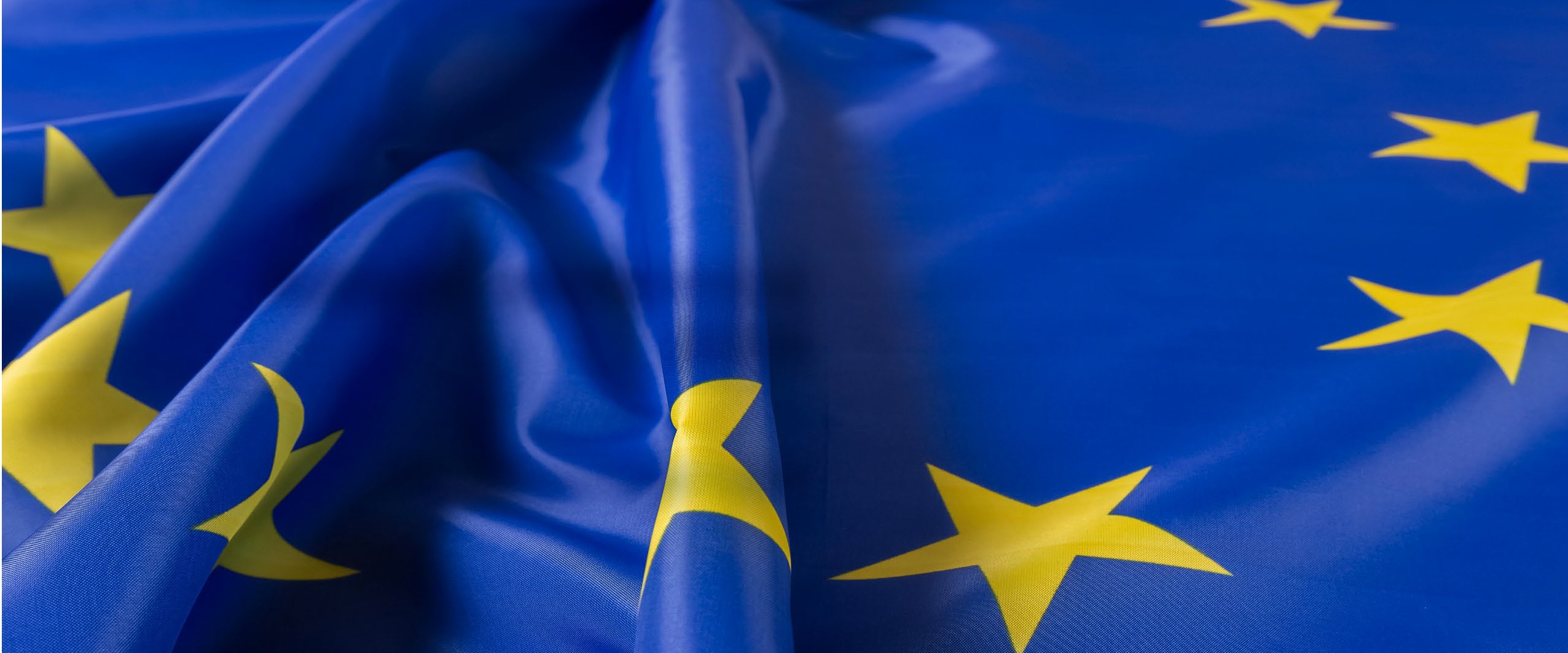 Wapperende vlag van de Europese Unie met gele sterren op blauwe achtergrond, symbool voor Europese samenwerking en regelgeving.