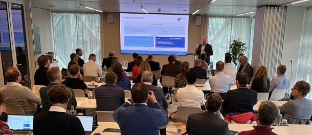 Groep professionals volgt een presentatie in een vergaderruimte, terwijl spreker uitleg geeft bij slides over strategie en beleid.