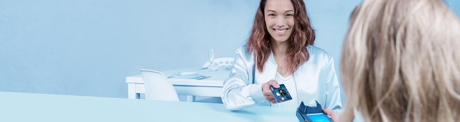 Vrouw overhandigt glimlachend haar betaalpas aan een medewerker die een pinterminal vasthoudt, tijdens een rustige contactloze betaling aan tafel.