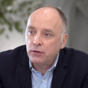 Persvoorlichter in donker colbert en lichtblauw overhemd in gesprek in een lichte, professionele kantooromgeving.